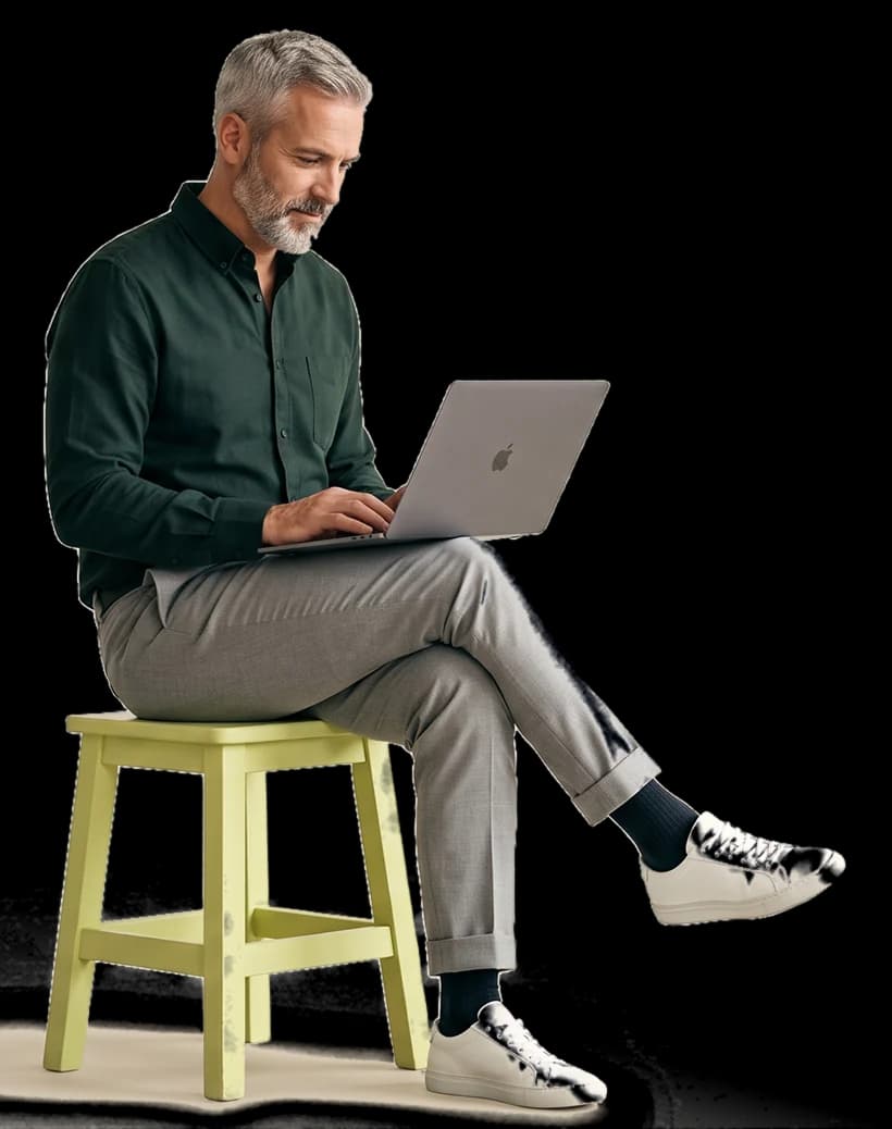 A man sitting on a lime stool, working on a laptop